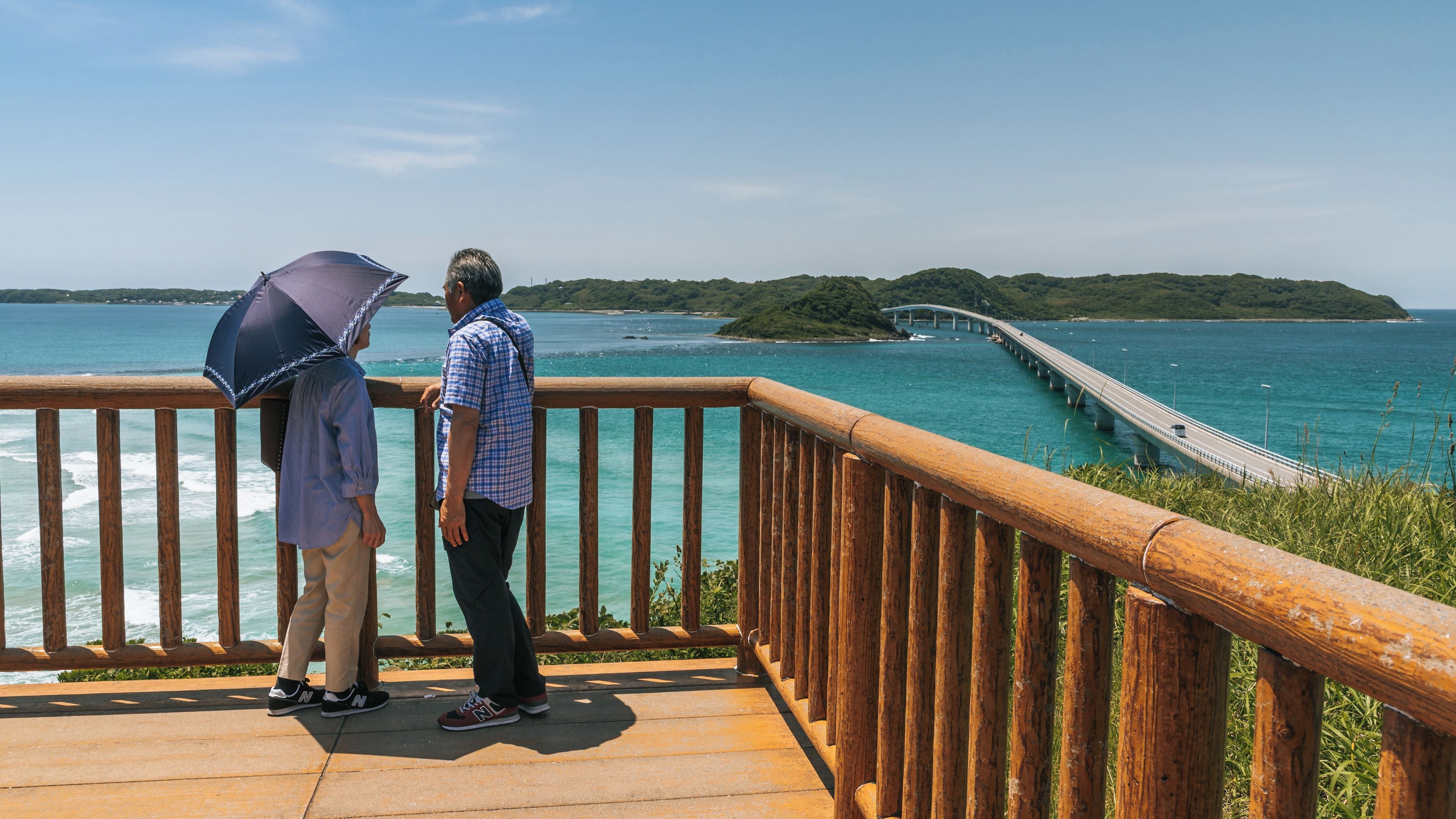 A wooden deck overlooking a coastal area with a bridge and distant green hills.