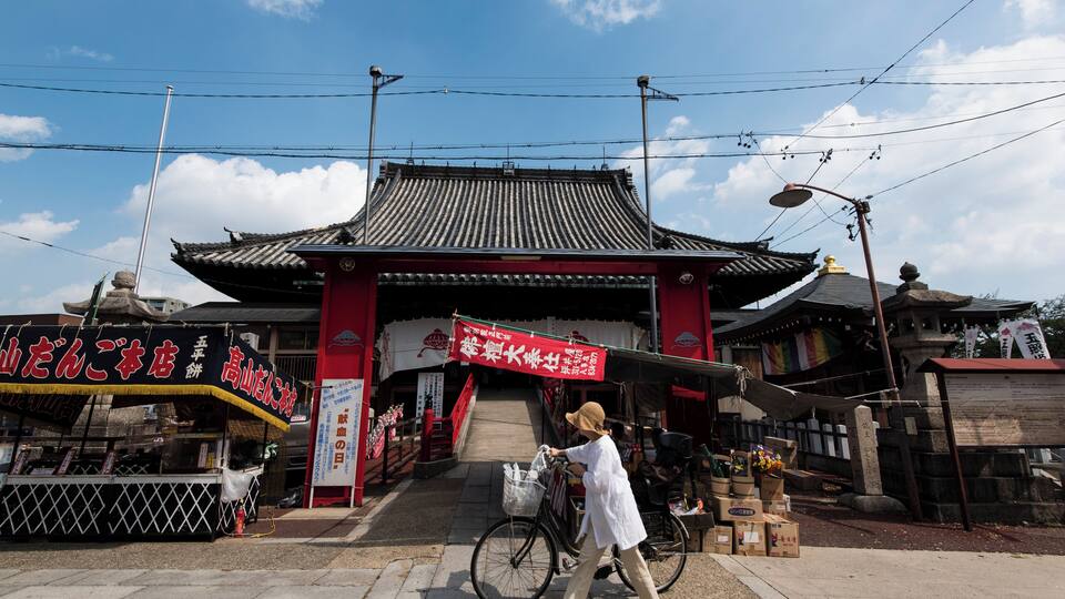 Ein traditionelles japanisches Tor mit einem roten Torii, ein Fahrrad mit Korb und ein Straßenverkaufswagen.