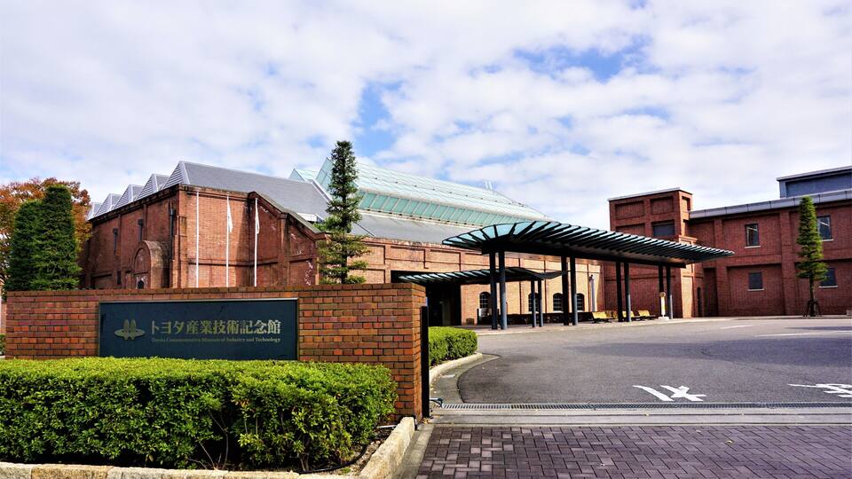 A building with a sign reading "Toyota Commemorative Museum of Industry and Technology" and a covered entrance.