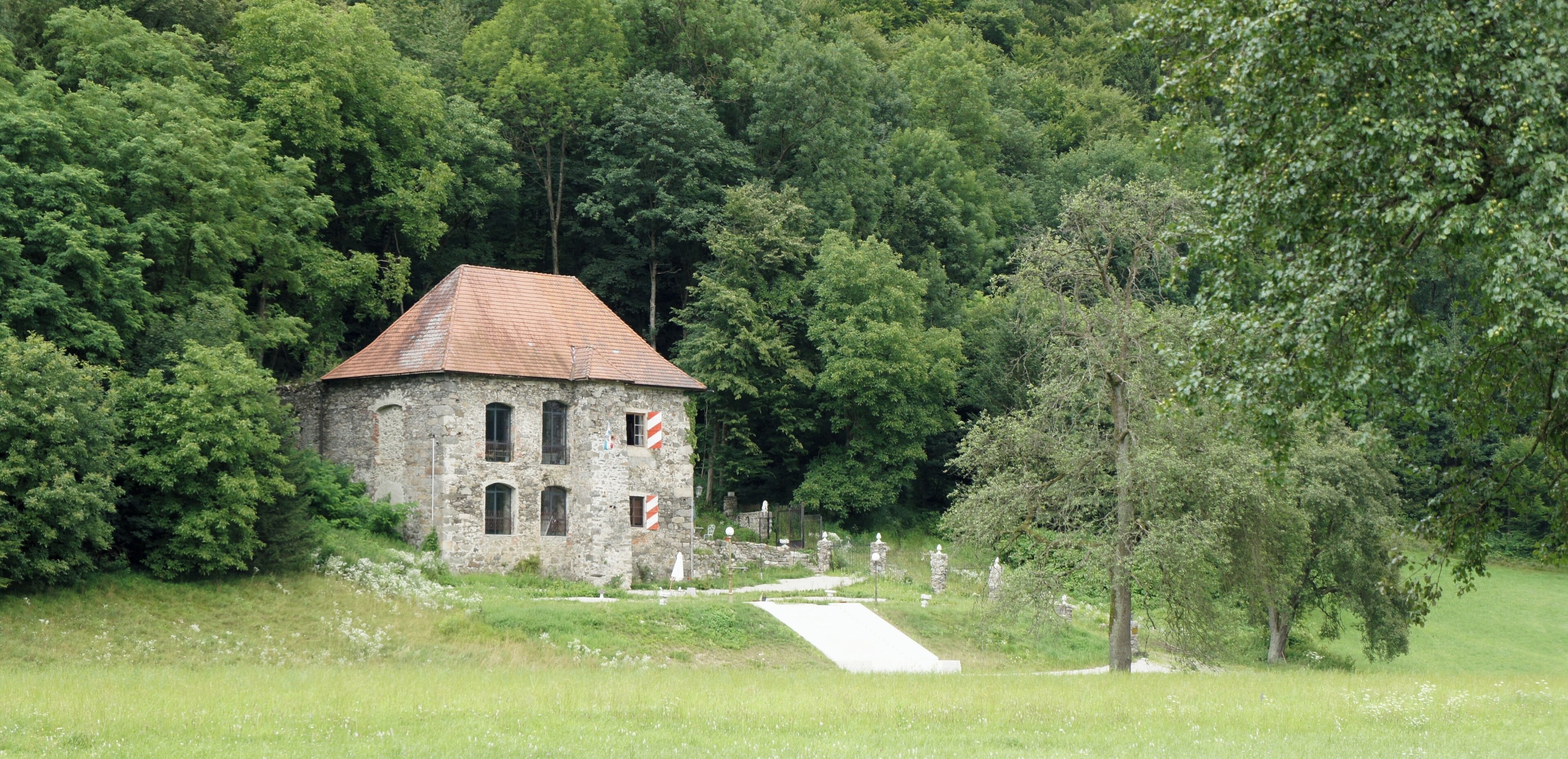A stone building with a tiled roof surrounded by lush greenery and trees.