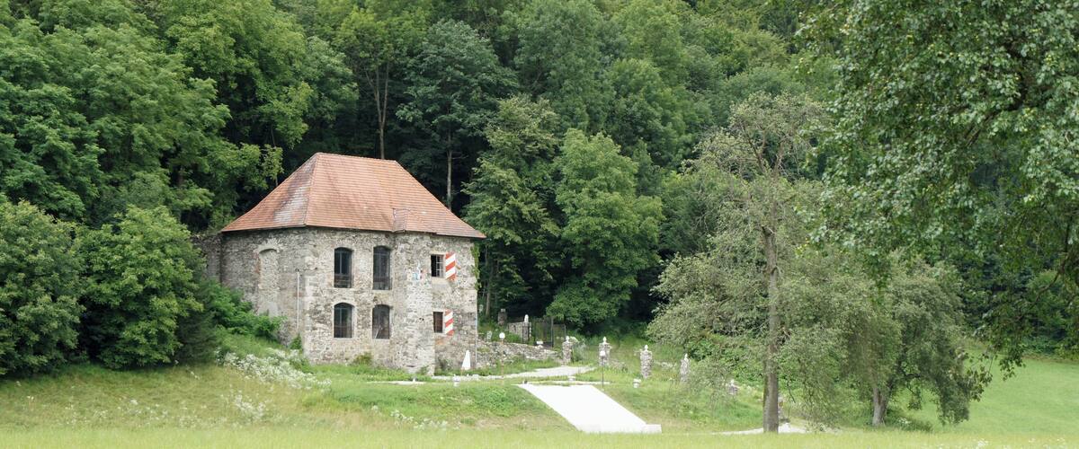 A stone building with a tiled roof surrounded by lush greenery and trees.