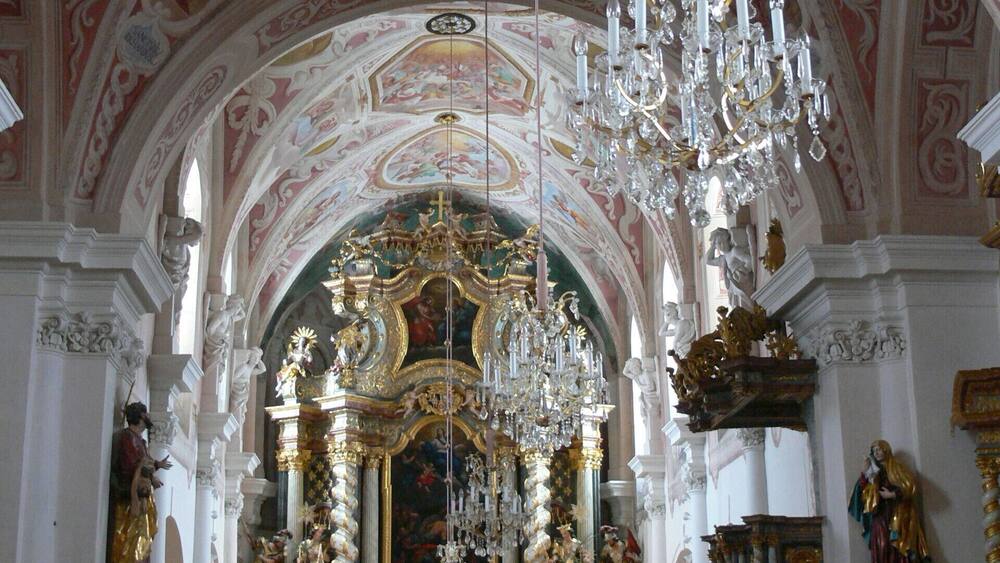 An ornate church interior with a large chandelier, a decorated altar, and a statue of a woman holding a child.