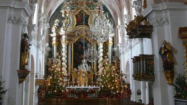 An ornate church interior with a large chandelier, a decorated altar, and a statue of a woman holding a child.