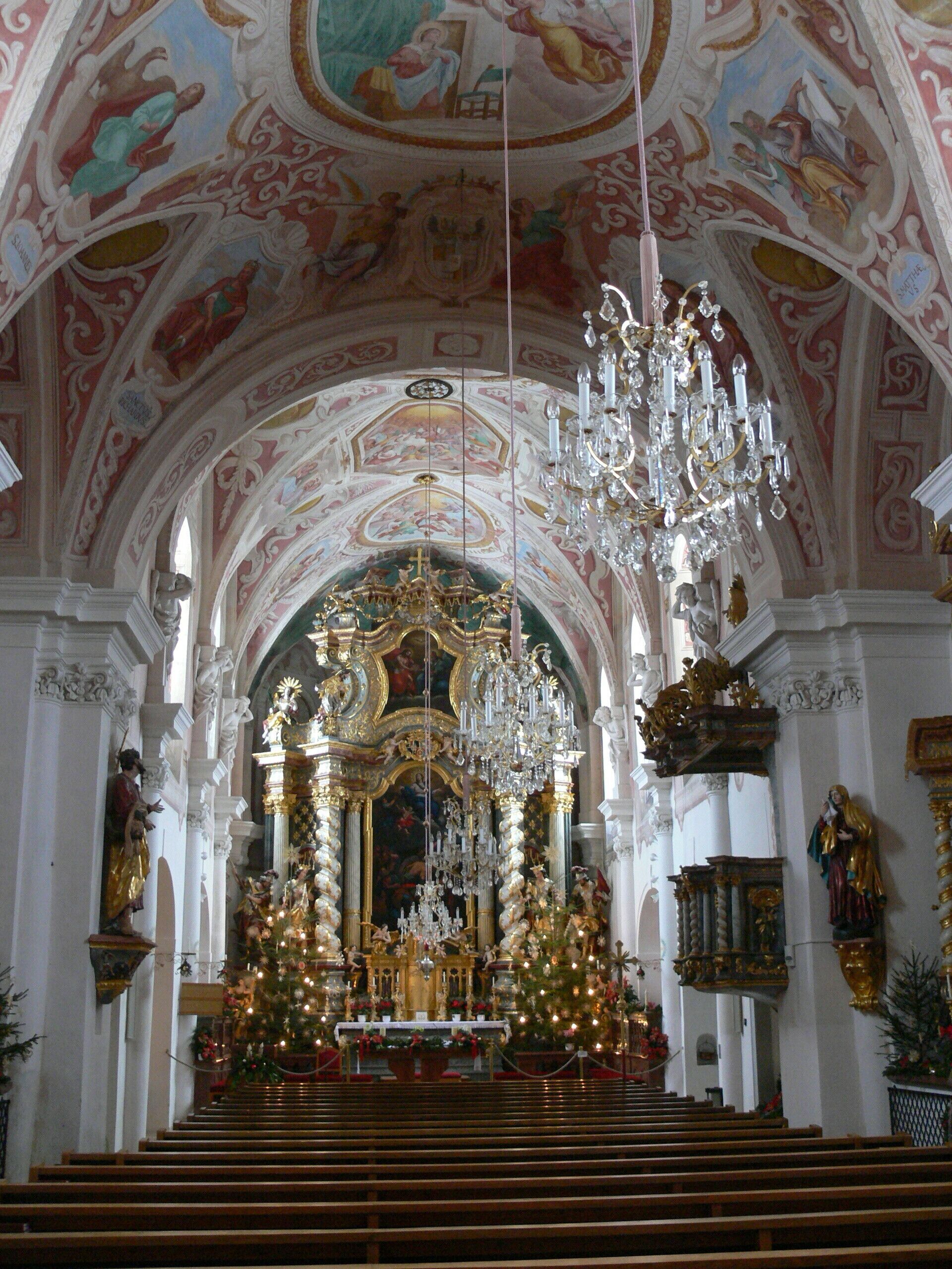 An ornate church interior with a large chandelier, a decorated altar, and a statue of a woman holding a child.