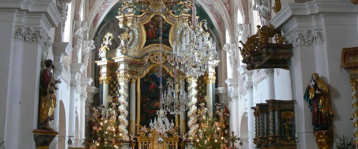 An ornate church interior with a large chandelier, a decorated altar, and a statue of a woman holding a child.