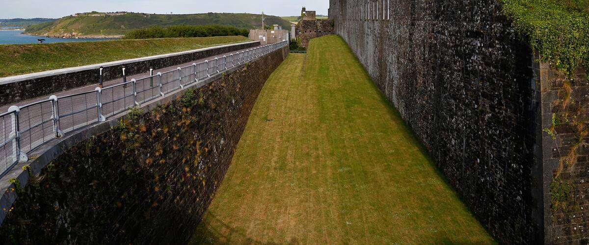 A stone wall with a grassy path alongside a body of water.