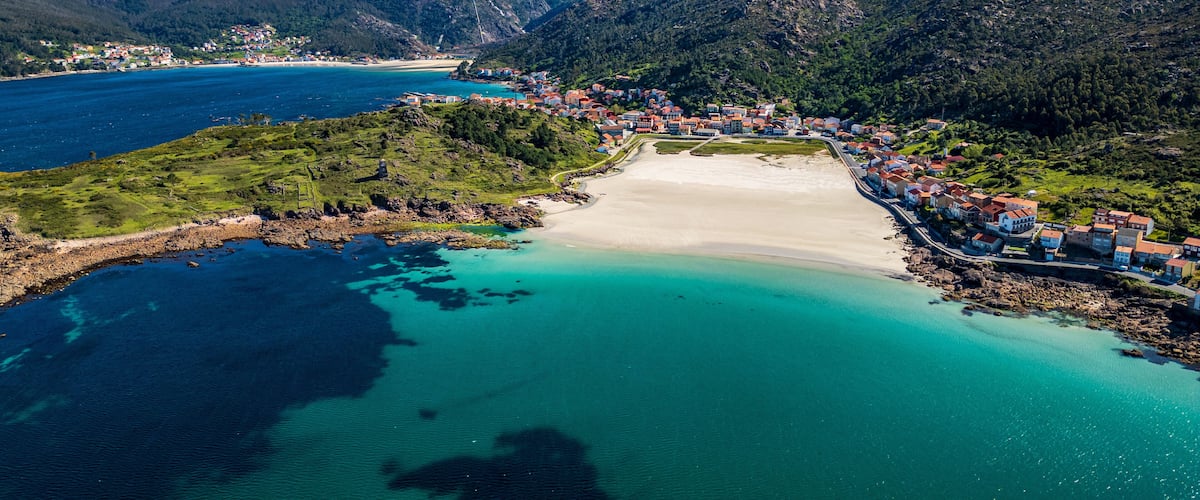 A coastal town with a beach, wind turbines, and mountainous terrain.