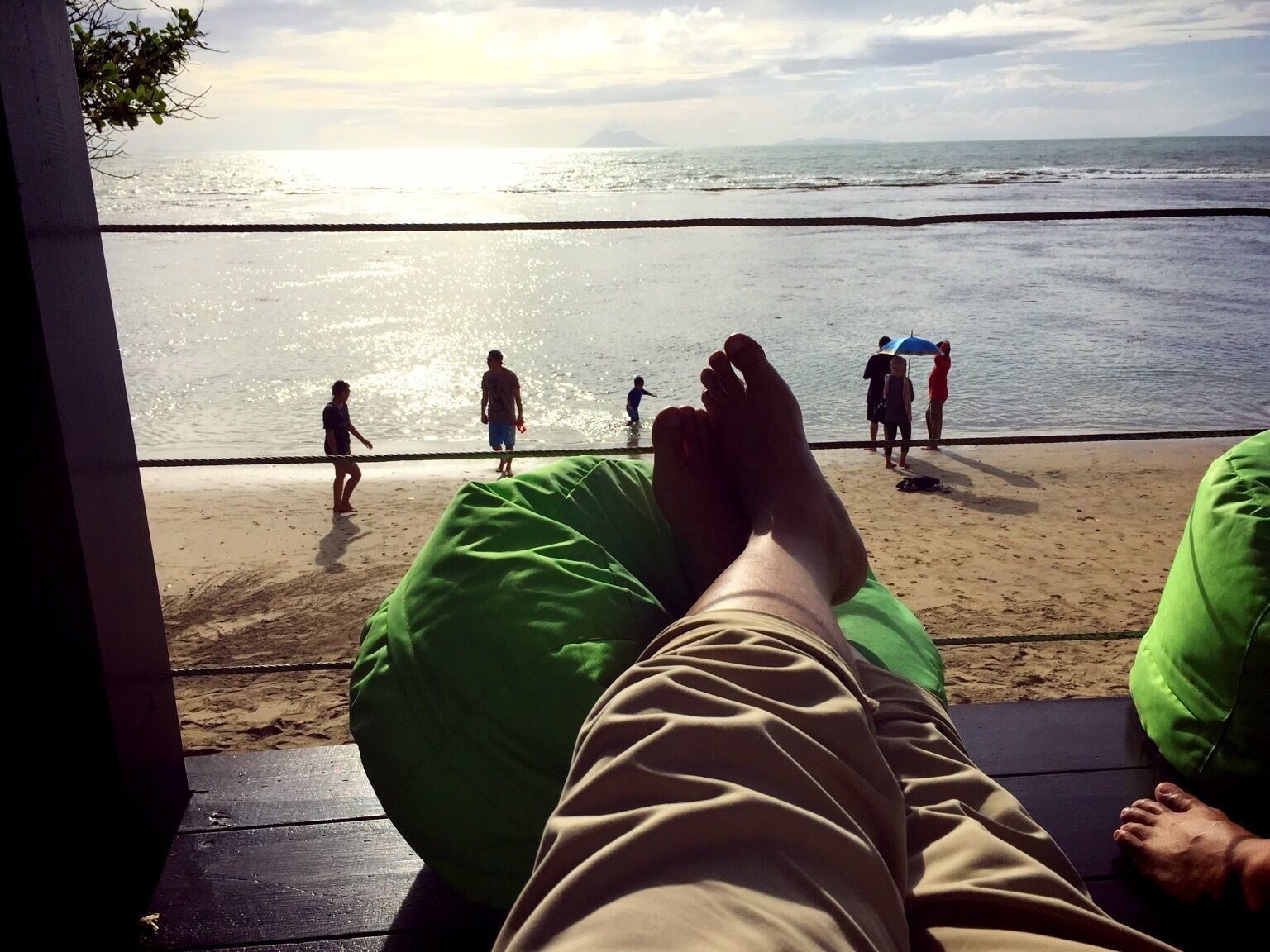 A beach scene with a person reclining on a bench, facing the ocean.