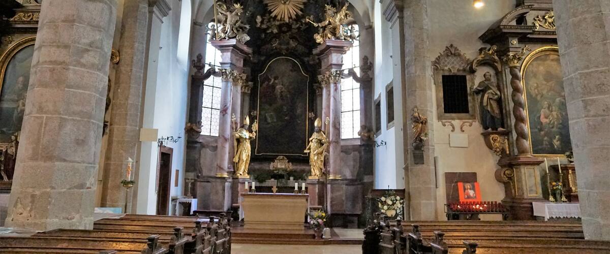 An ornate church interior with high vaulted ceilings, large columns, and religious statues.