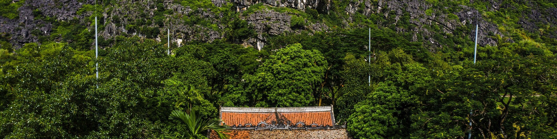 Um templo tradicional rodeado por vegetação exuberante e montanhas rochosas.