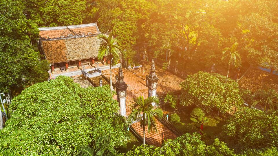 A traditional temple with a tiled roof, surrounded by lush greenery and palm trees.