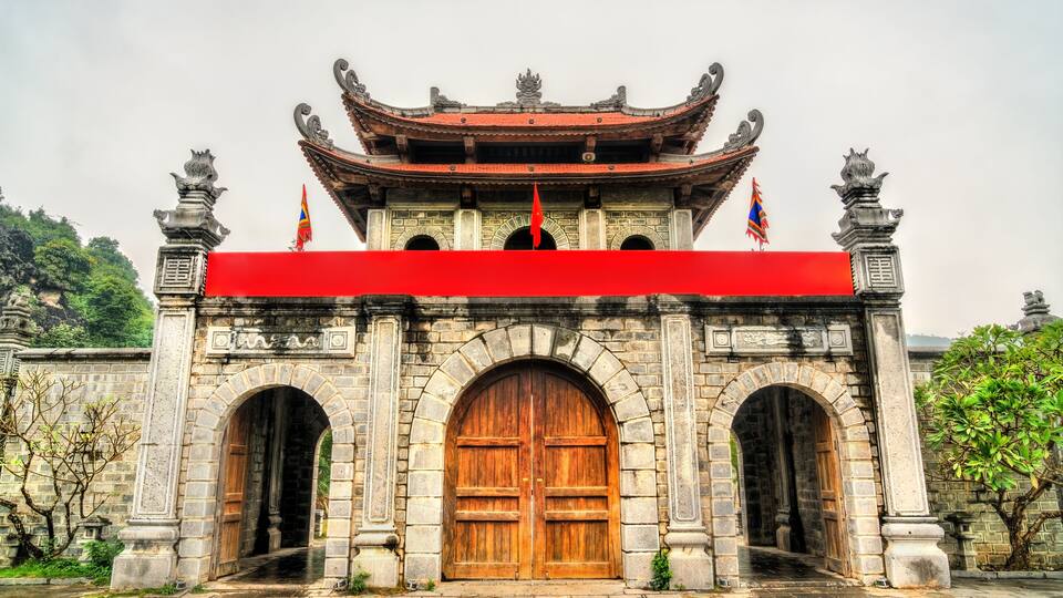 A traditional gate with a red awning, stone pillars, and a tiled roof.