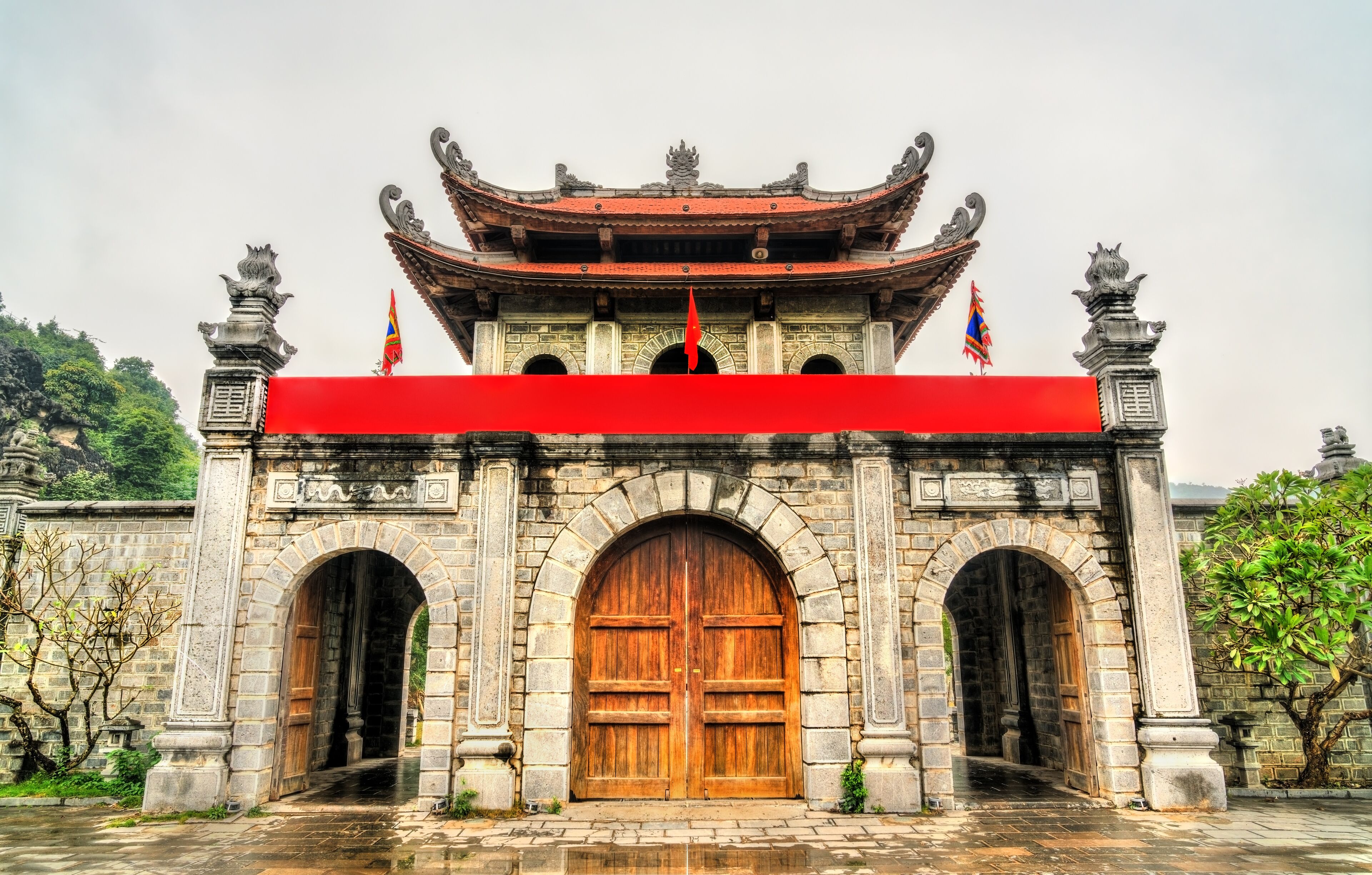 A traditional gate with a red awning, stone pillars, and a tiled roof.