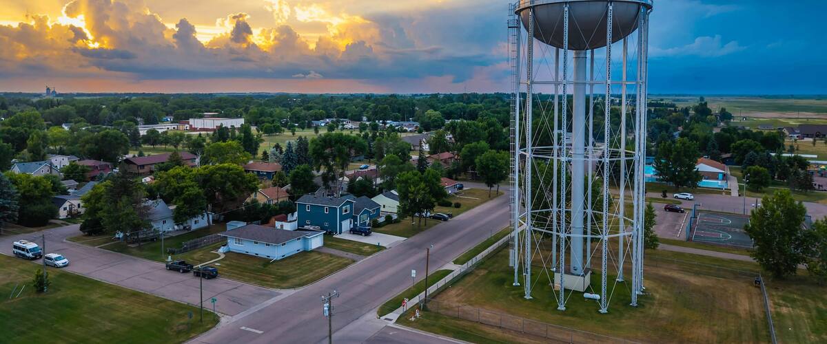 A water tower labeled "DeVilsLake" in a suburban area with houses, roads, and a cloudy sky.