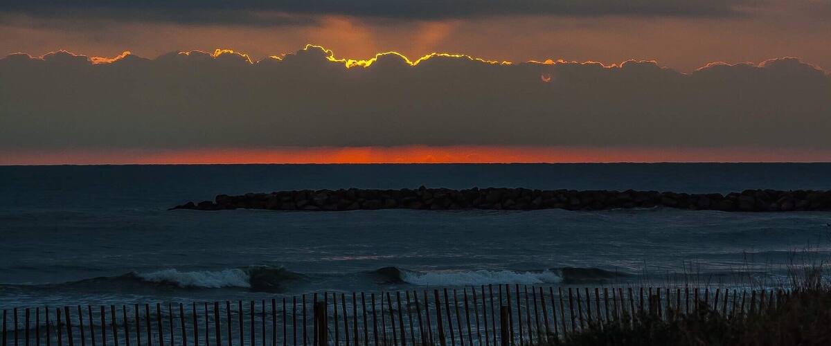 A sunset over the ocean with a rocky breakwater in the foreground.