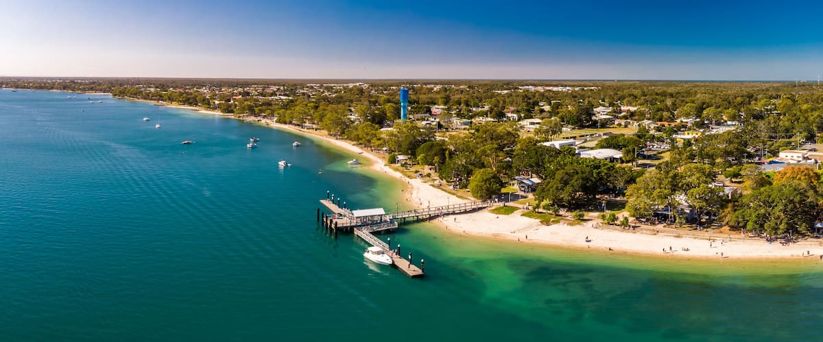 A coastal town with a pier extending into turquoise waters, surrounded by lush greenery and residential areas.