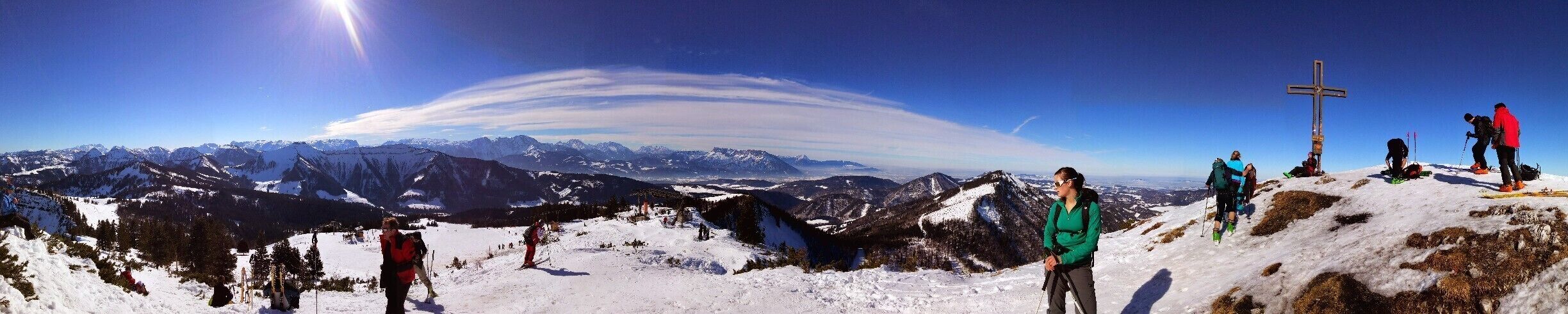 A snowy mountain landscape with skiers and a cross on a hill.