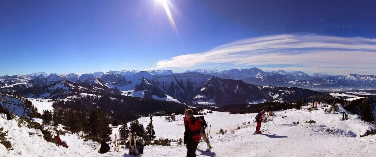 A snowy mountain landscape with skiers and a cross on a hill.