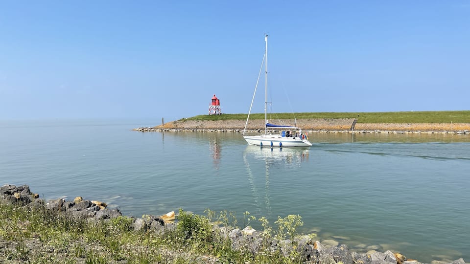 A calm lake with a sailboat anchored near a lighthouse on a rocky shore.