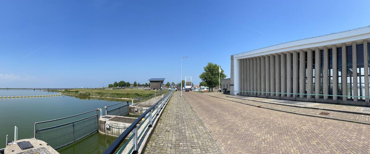 A waterfront promenade with a modern building, a canal, and a distant pier.