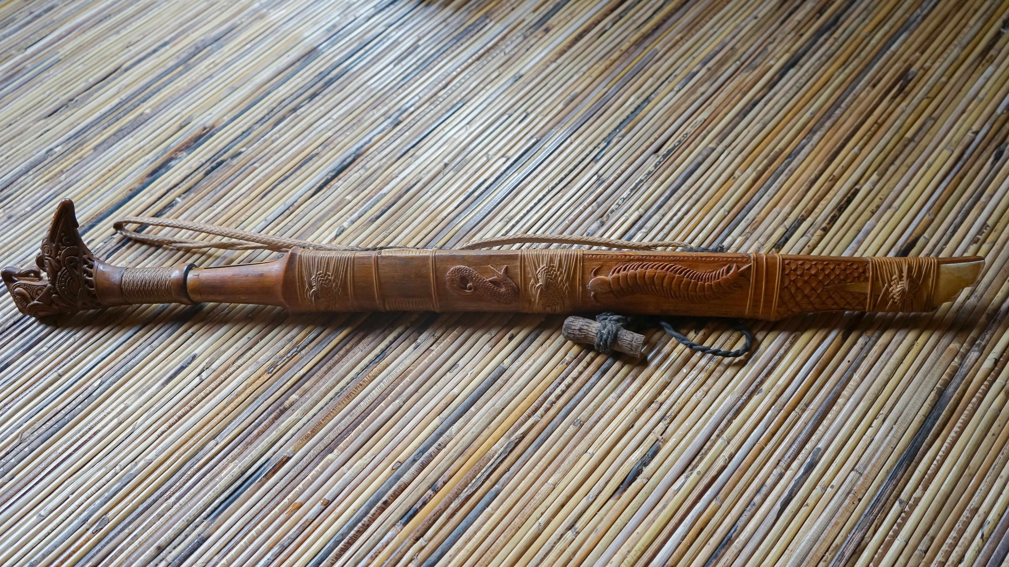 A wooden walking stick with intricate carvings and a rope handle, lying on a bamboo mat.