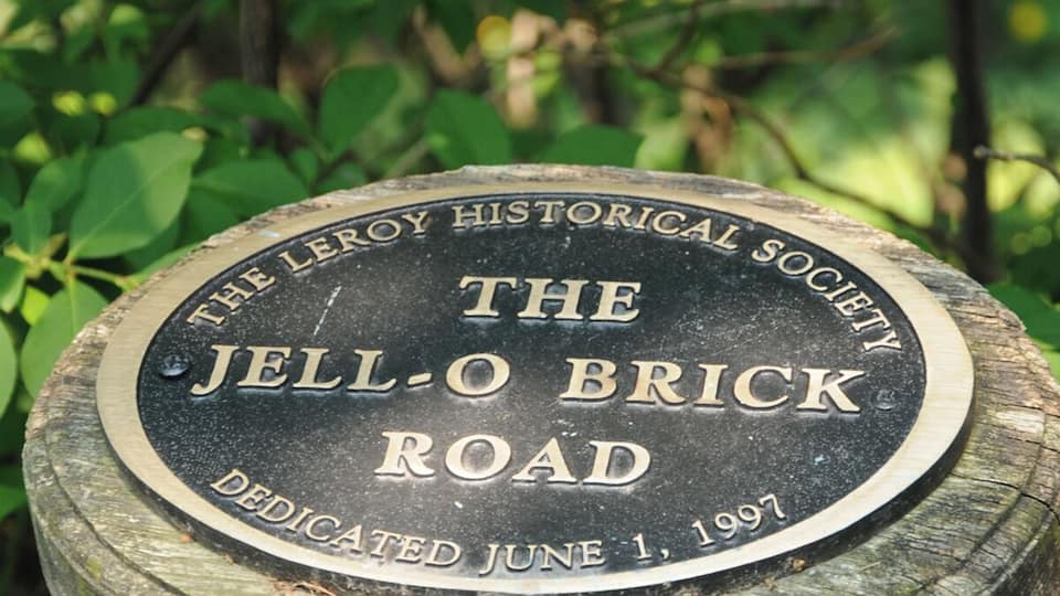 A plaque on a post with the text "The Leroy Historical Society Jell-O Brick Road Dedicated June 1, 1997".