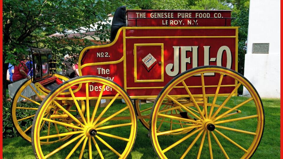 A vintage carriage with yellow wheels and a red body, labeled "JELLO" and "The Genesee Pure Food Co."