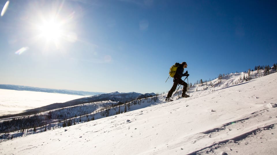 A skier on a snowy mountain slope with a clear sky and distant mountains.