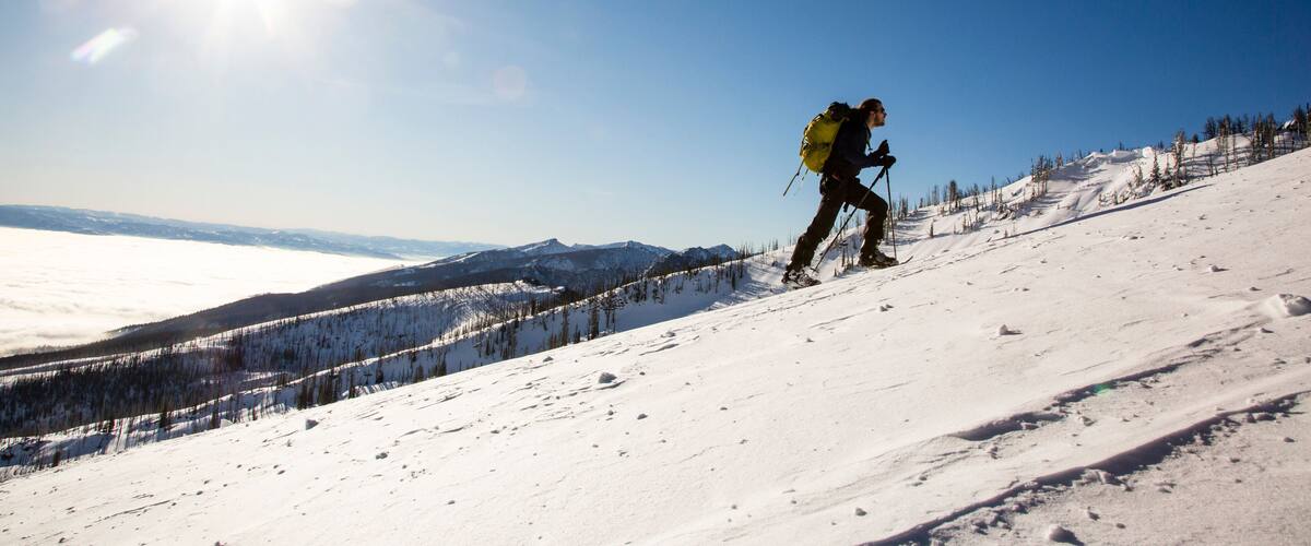 A skier on a snowy mountain slope with a clear sky and distant mountains.