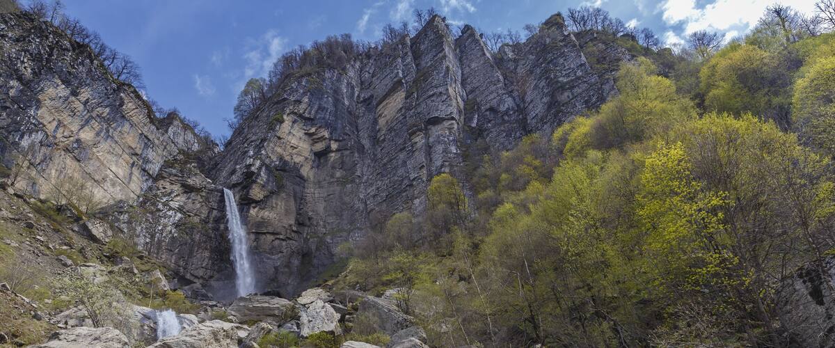 A waterfall cascading down a rocky cliff surrounded by lush greenery.
