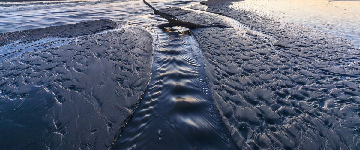 A beach at sunset with calm waves and a clear sky.