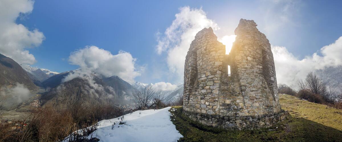 A stone ruin with a clear sky and snow-covered mountains in the background.