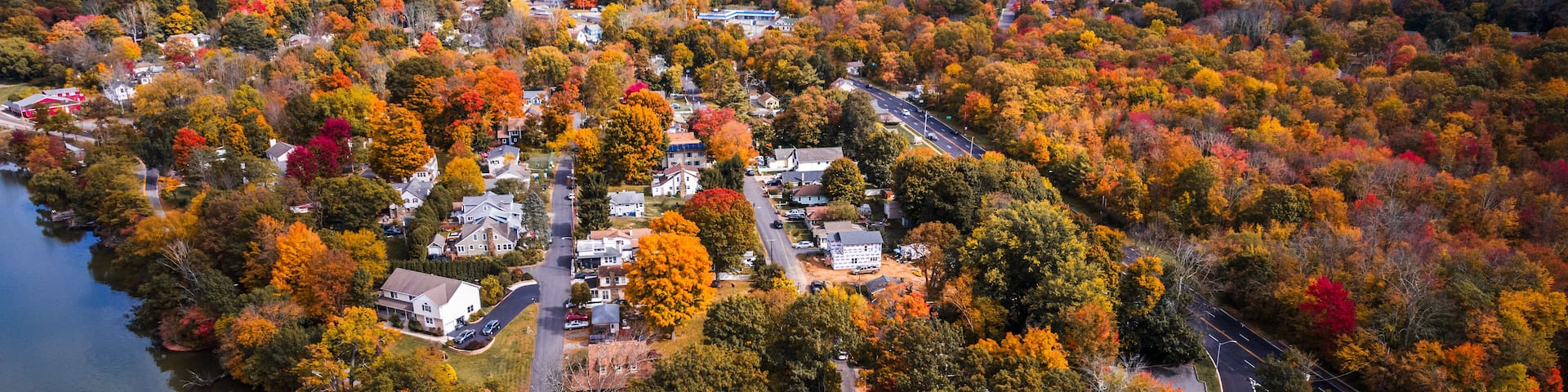 An aerial view of a lakeside community with autumn foliage, surrounded by hills.