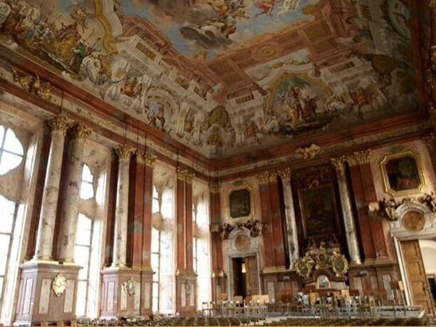 An ornate room with classical architecture, including columns, a detailed ceiling fresco, and a large altar.