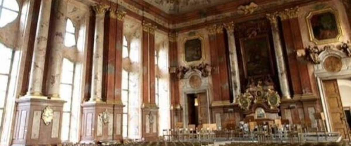 An ornate room with classical architecture, including columns, a detailed ceiling fresco, and a large altar.