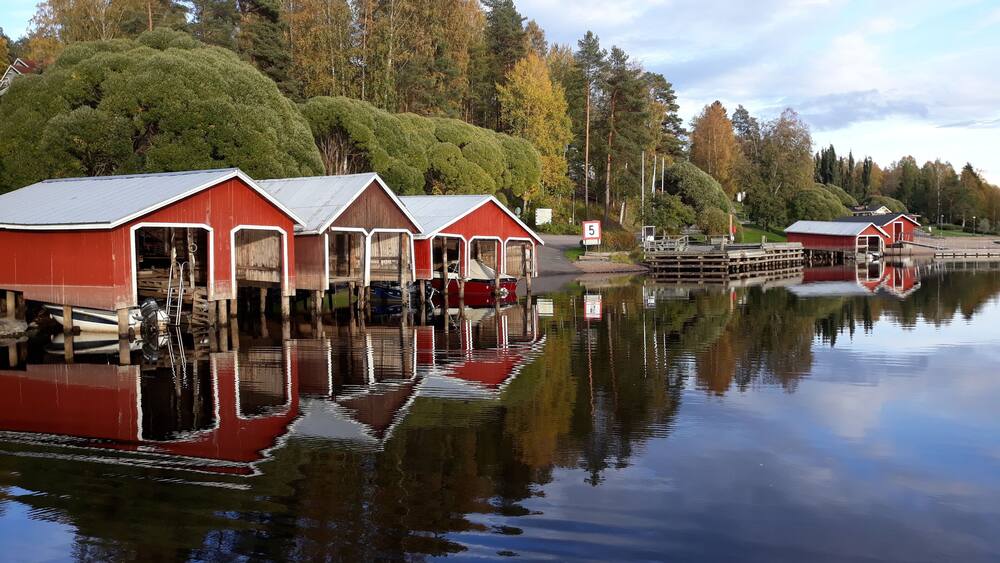 A calm lake with red wooden boathouses and a dock.