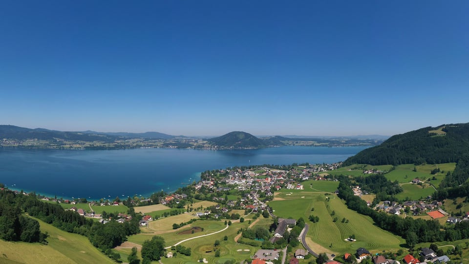 A lake surrounded by hills and a small town with green fields and houses.