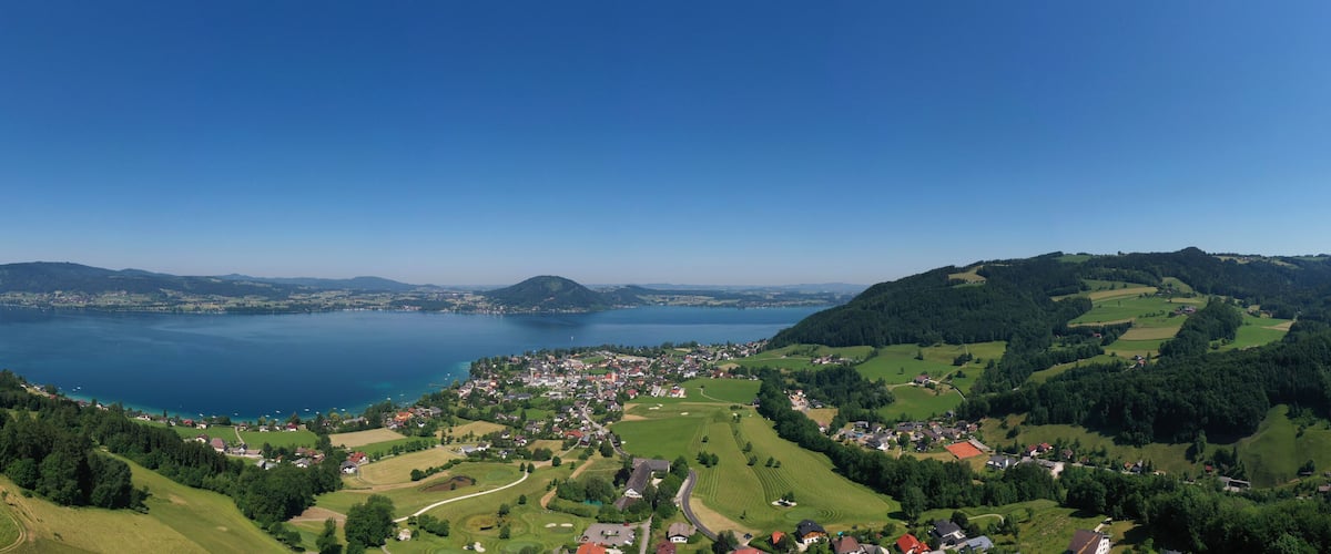 A lake surrounded by hills and a small town with green fields and houses.