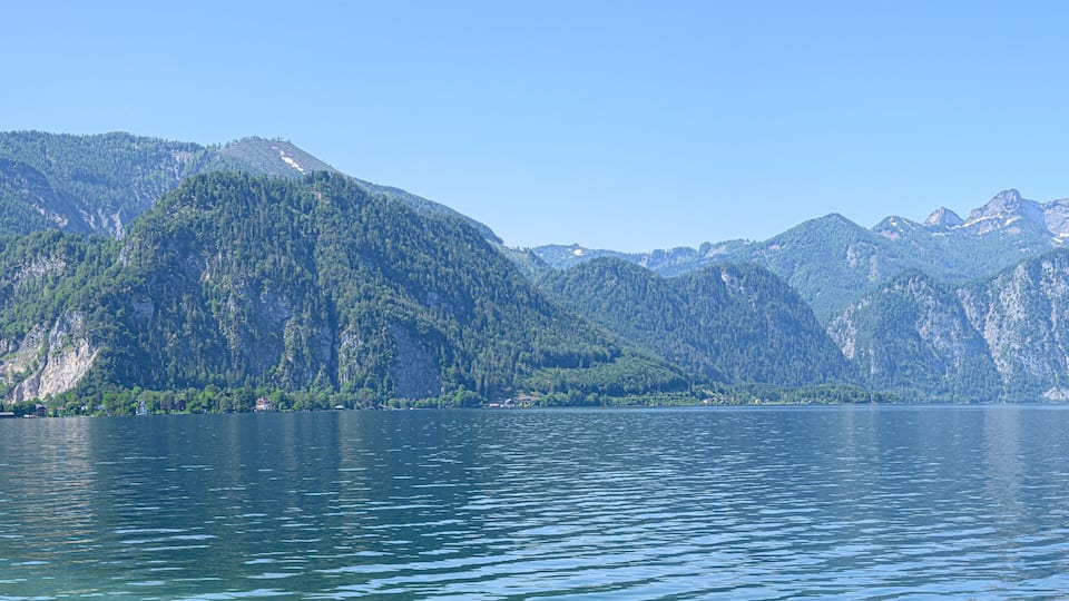 A calm lake surrounded by forested mountains under a clear sky.