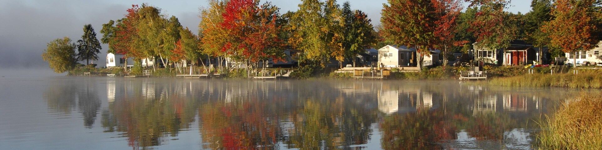Um lago calmo refletindo árvores e edifícios.
