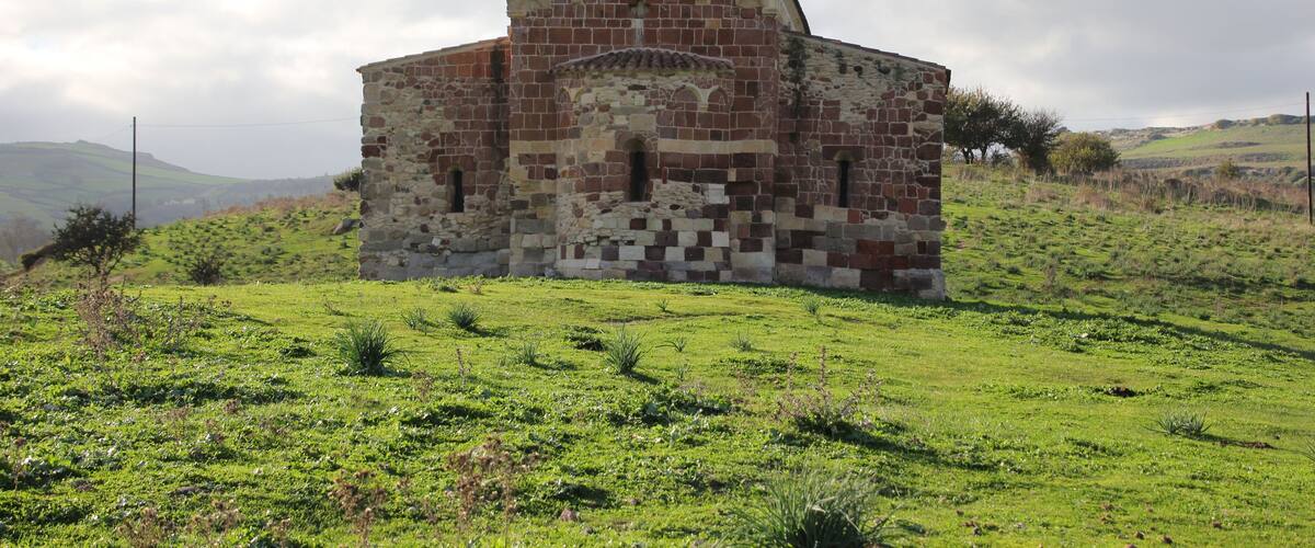 A stone building with a triangular roof in a grassy field.