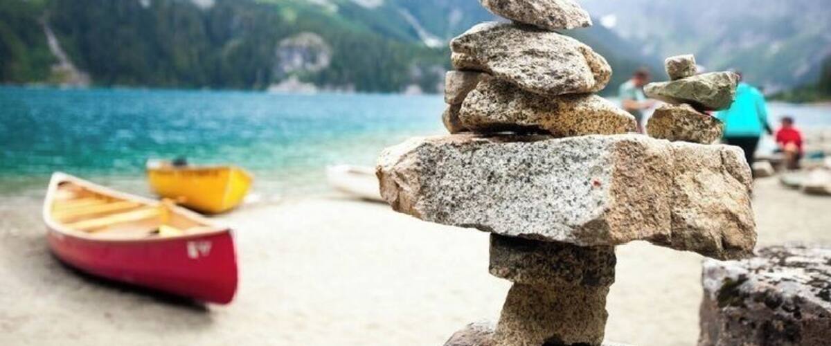 A stack of rocks on a beach with a lake and mountains in the background.