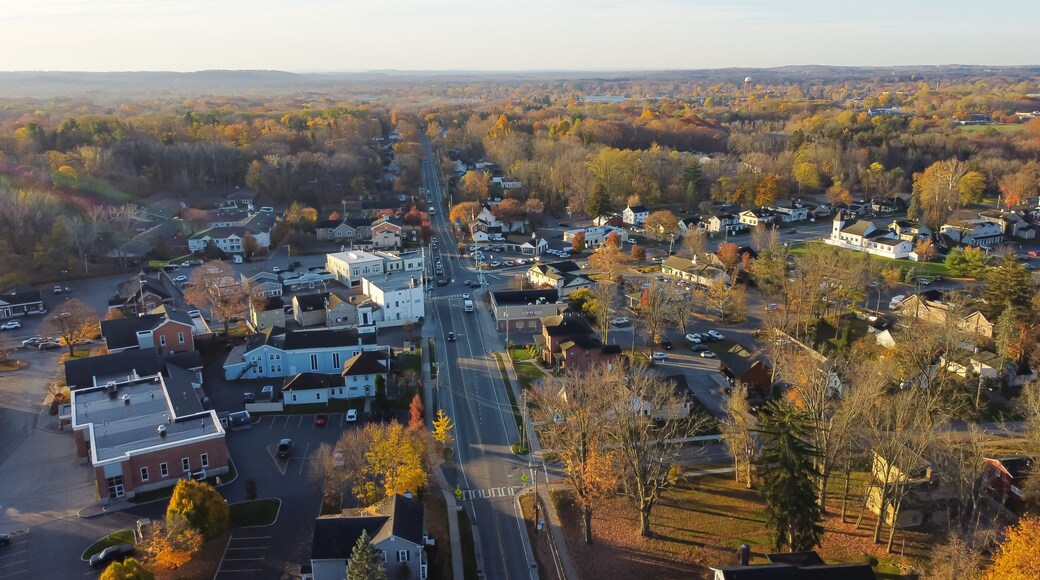 Aerial view Penfield town with local business, residential houses, churches along Five Mile Line Street lush green East Rochester in distant background, Upstate New York, USA