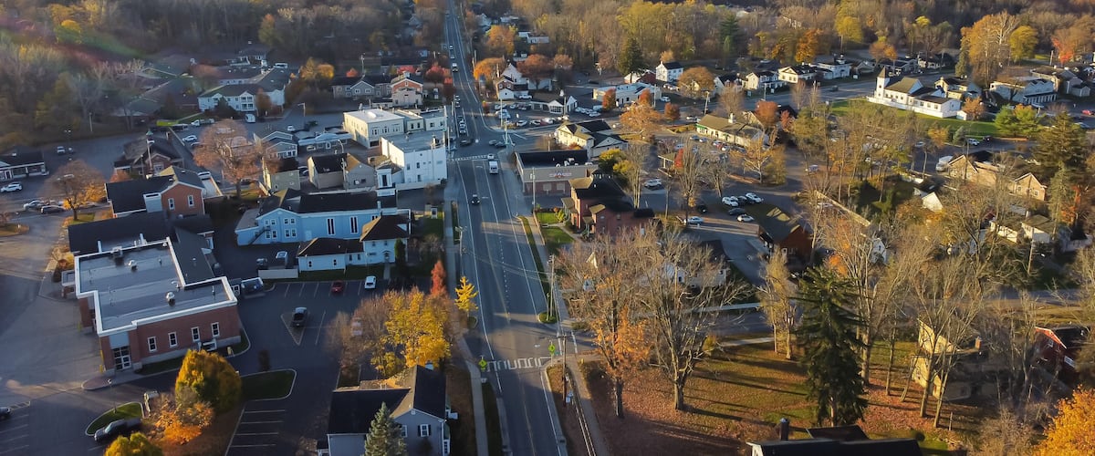 Aerial view Penfield town with local business, residential houses, churches along Five Mile Line Street lush green East Rochester in distant background, Upstate New York, USA