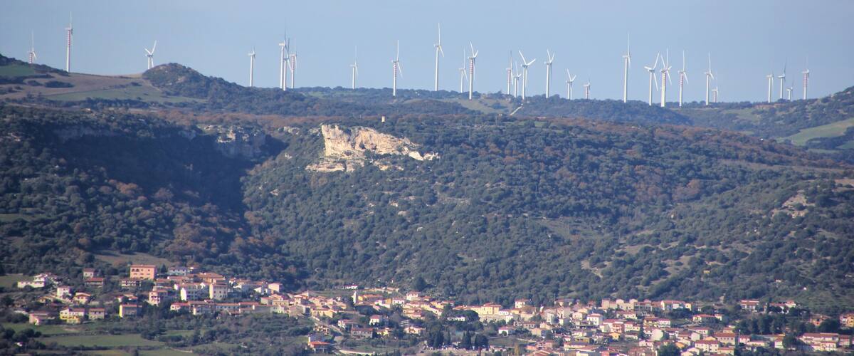 A town nestled in a valley with wind turbines in the background.