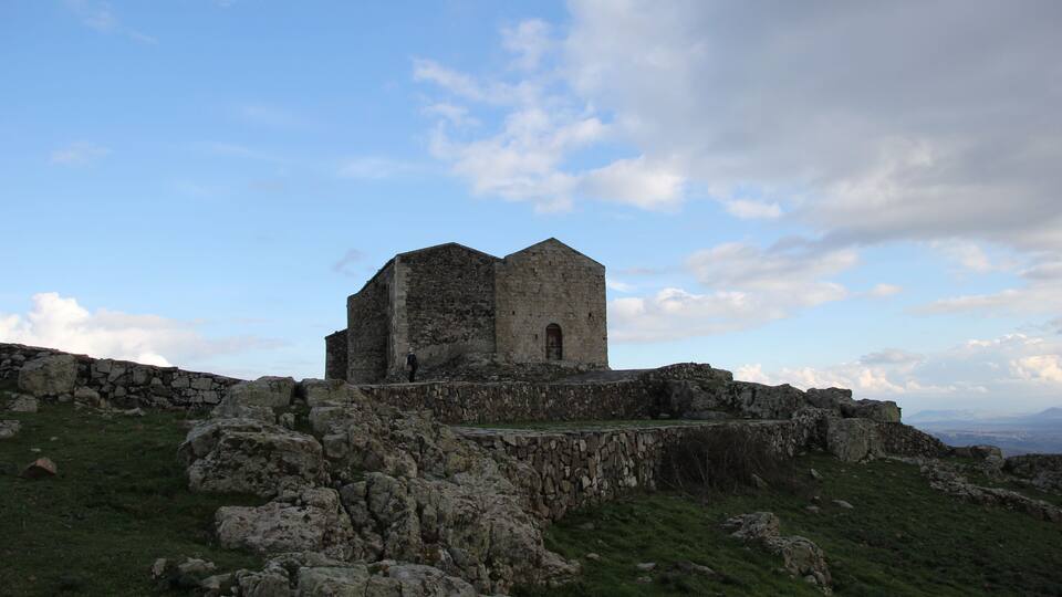 A stone building with a tower on a grassy hill.