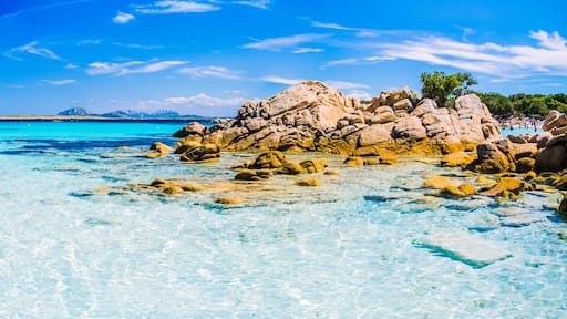 Mar turquesa y transparente con formaciones rocosas y montañas distantes bajo un cielo azul.