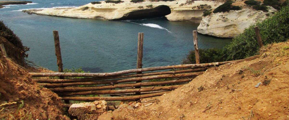 A coastal landscape with a sandy beach, rocky outcrops, and a wooden fence.