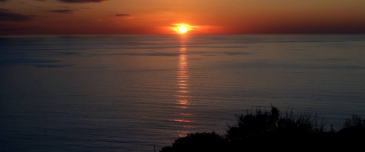 A sunset over a calm sea with a visible horizon line.
