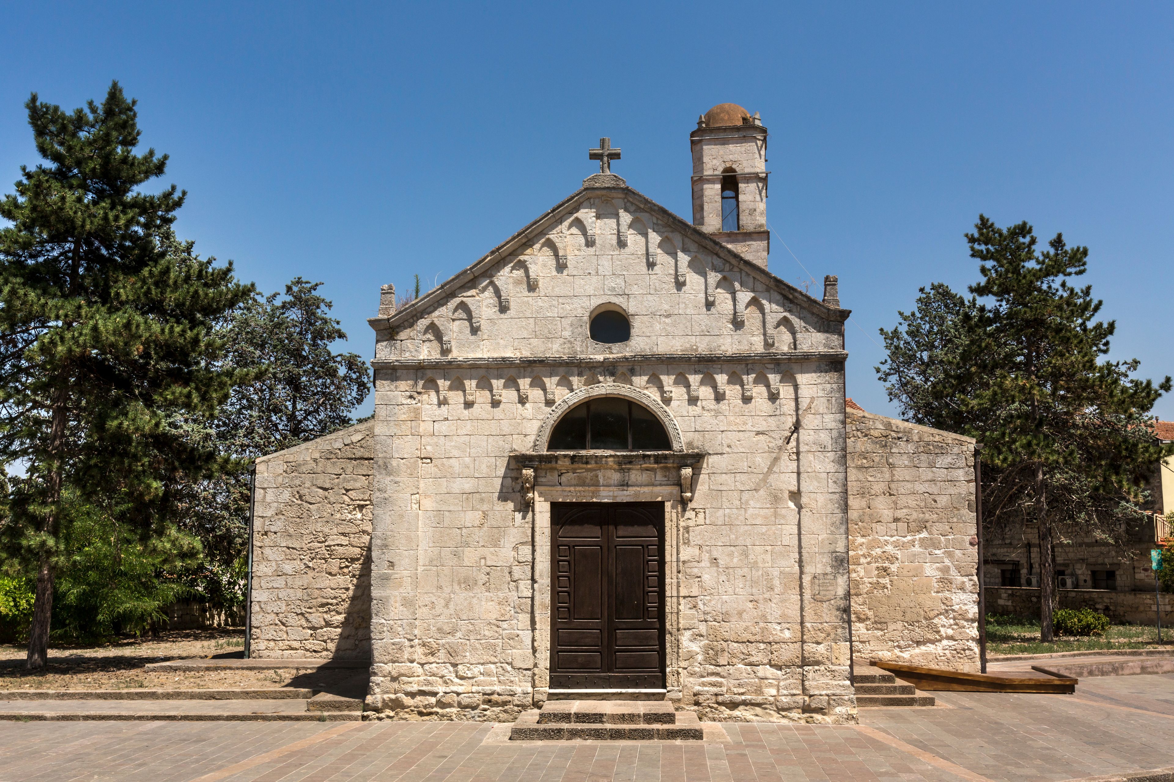 A stone church with a bell tower and a cross on top.